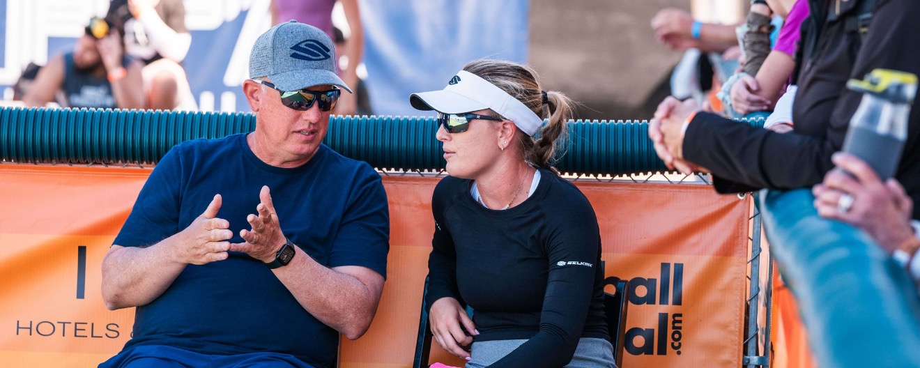 Vinnie Brascia talking to Mary Brascia sitting courtside at a pickleball match.