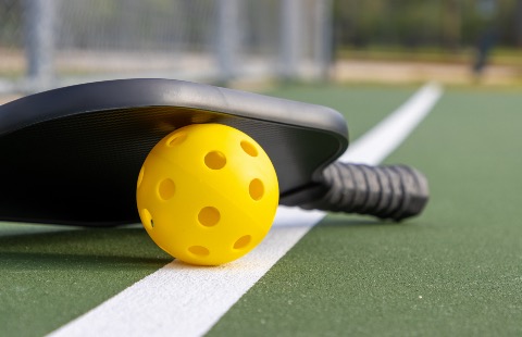 A pickleball and pickleball paddle on a pickleball court.