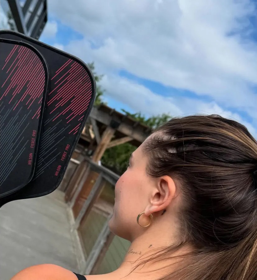 Back of Hailey's head and she's holding two pickleball paddles