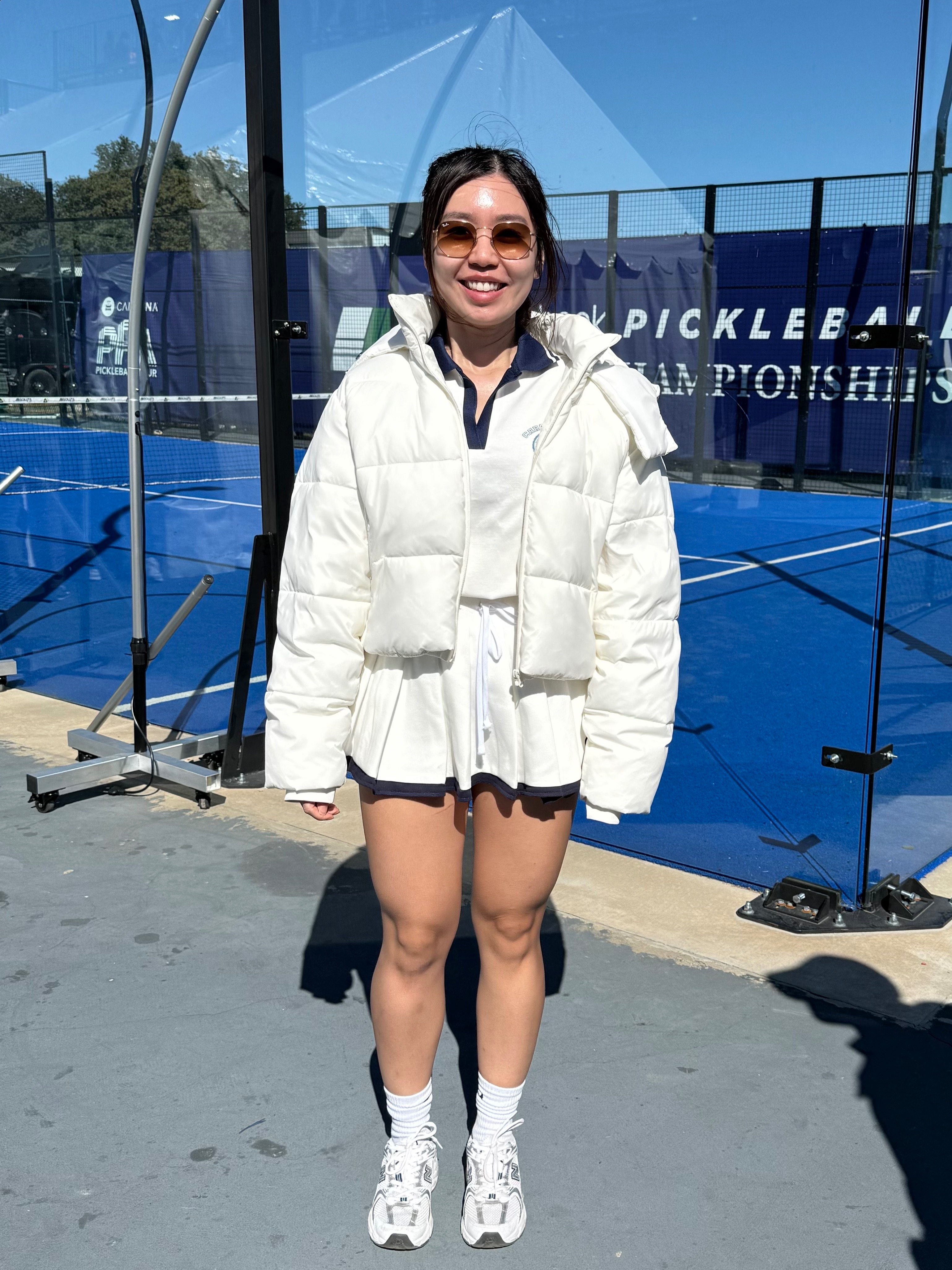 Trish in a white tennis dress and puffy wite jacket